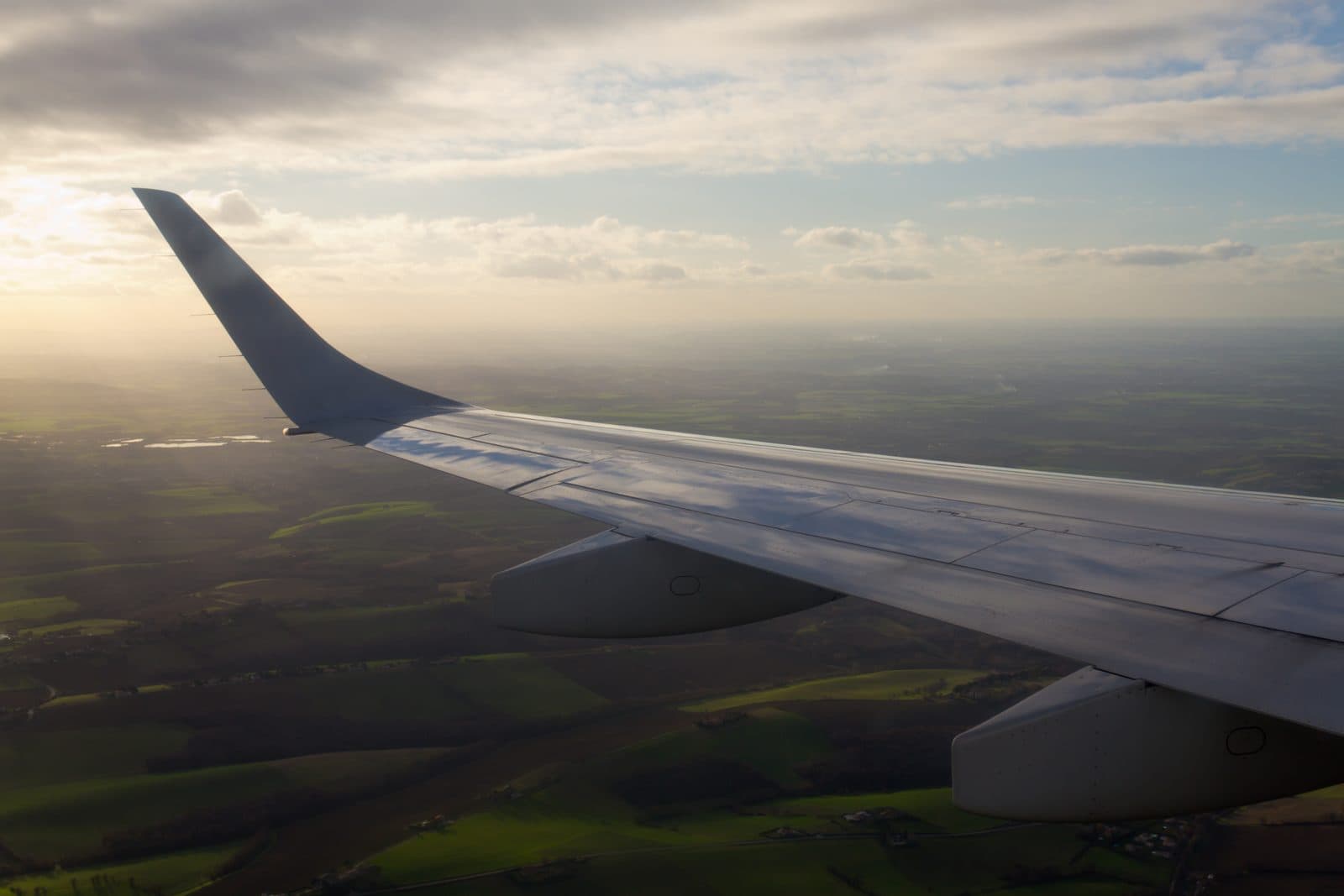 View of an aircraft wing above farmland at sunset